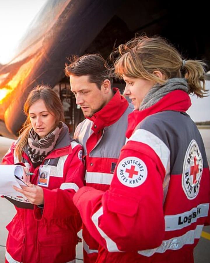 Drei Helferinnen und Helfer des Deutschen Roten Kreuzes besprechen vor einem Frachtflugzeug eine Ladeliste